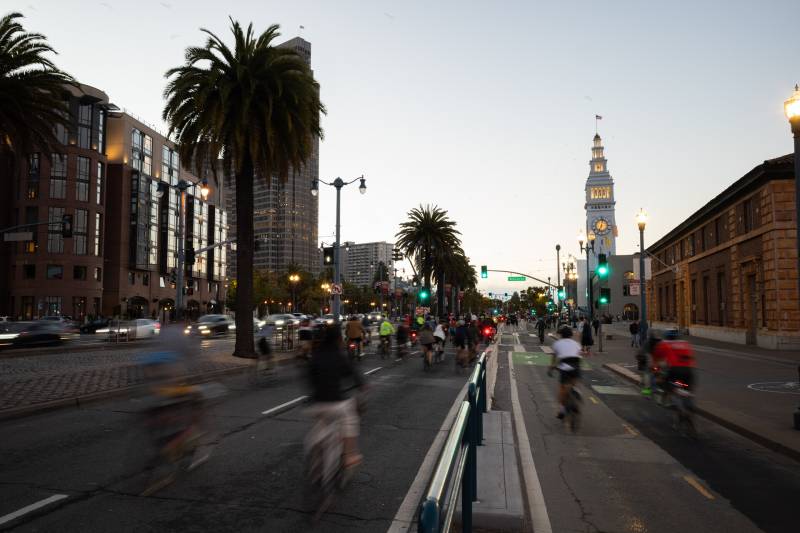 Bicyclists zoom by in bikes lanes going both directions along San Francisco's Embarcadero at sunset.