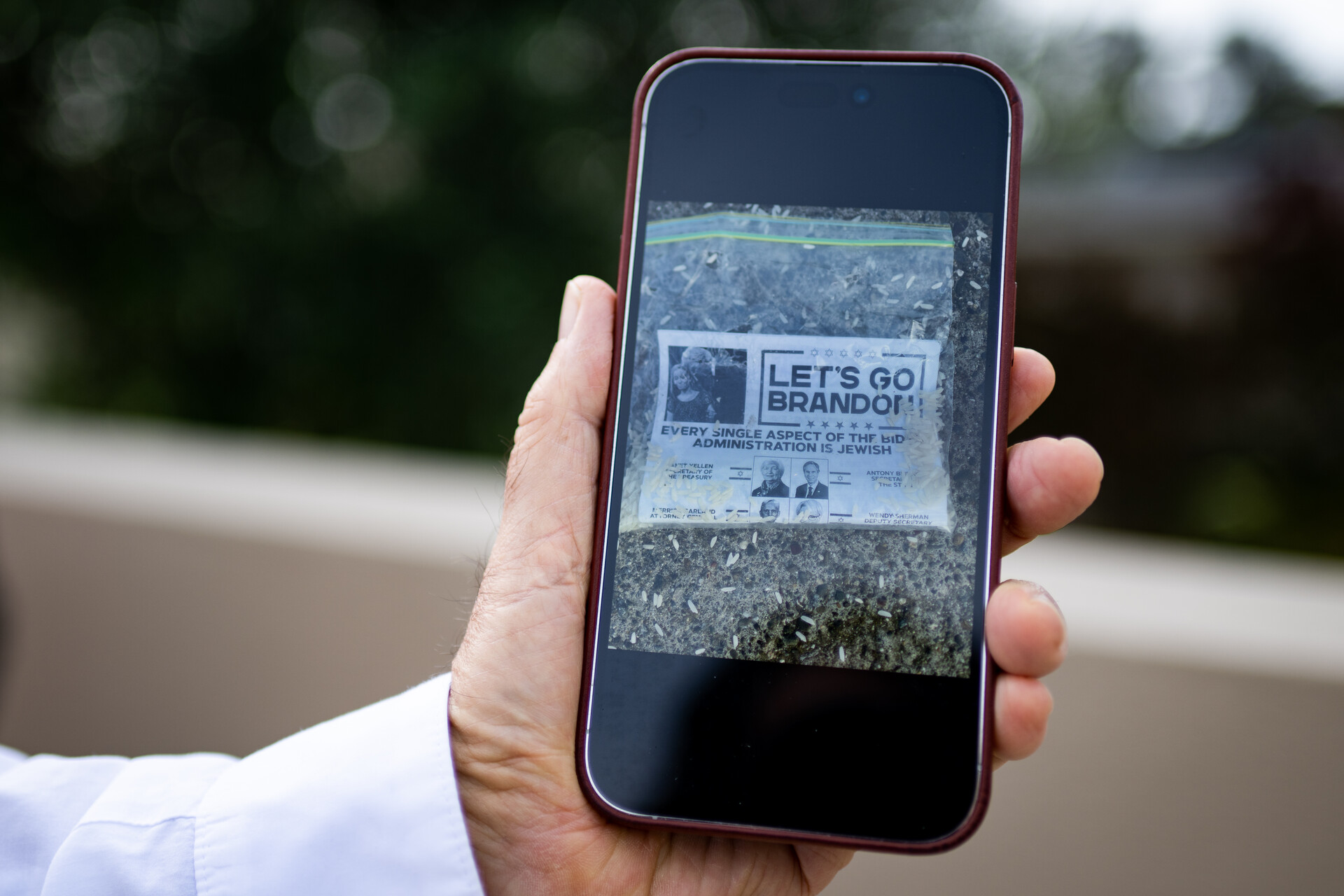 A closeup of a hand holding a smartphone displaying a photo of a black and white flyer contained in a zip lock bag