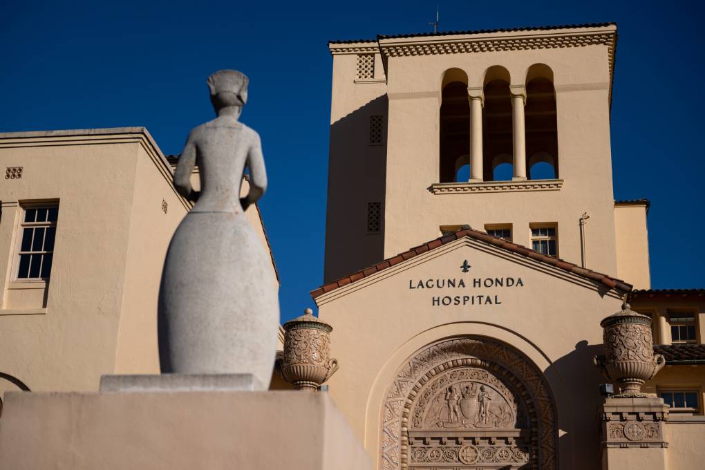 A view of the front of the large, sandy colored Laguna Honda Hospital in San Francisco, with a stone statue in the foreground