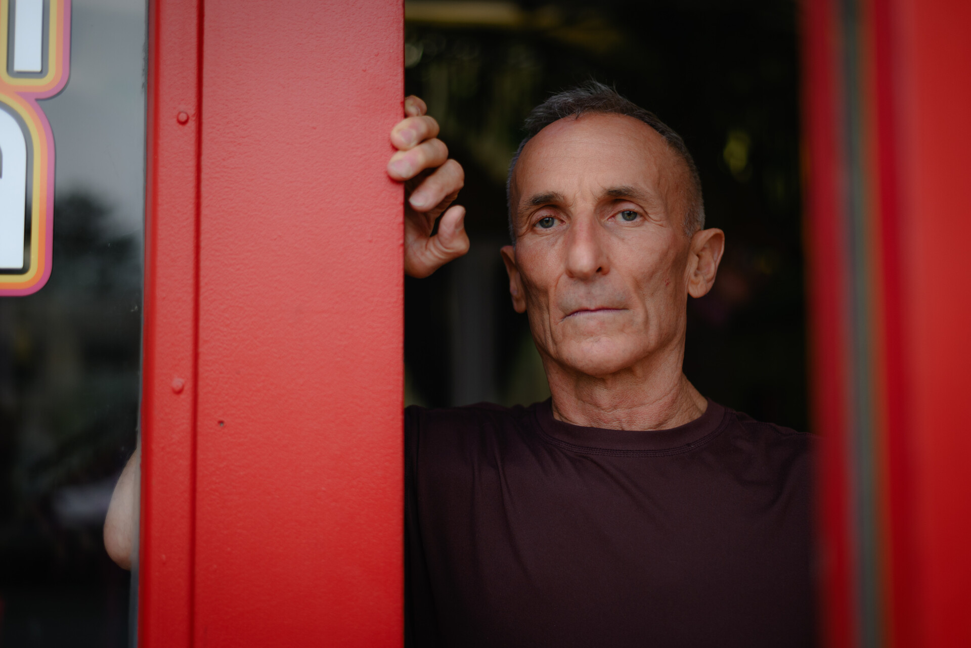 close-up portrait of a middle aged white man standing in a doorway, with one hand on the red-painted door frame
