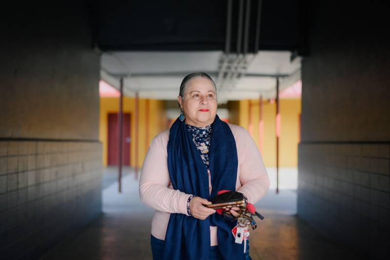 An older Latina woman stands in a school hallway looking off camera.