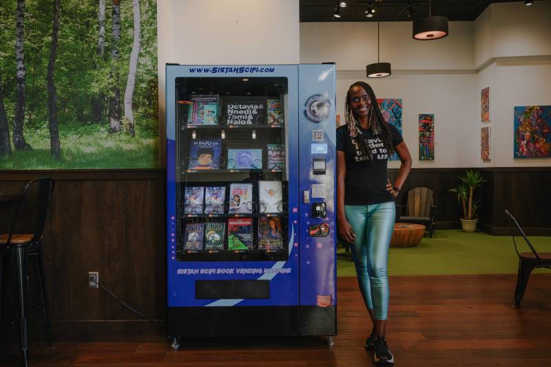 A woman stands next to a book vending machine.