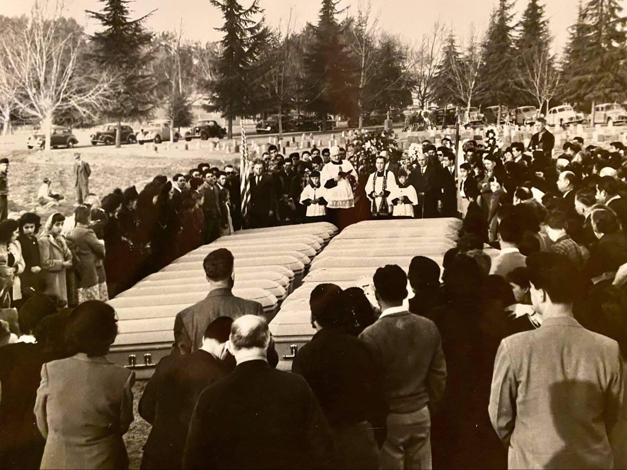 People gather around a large number of coffins at a funeral.