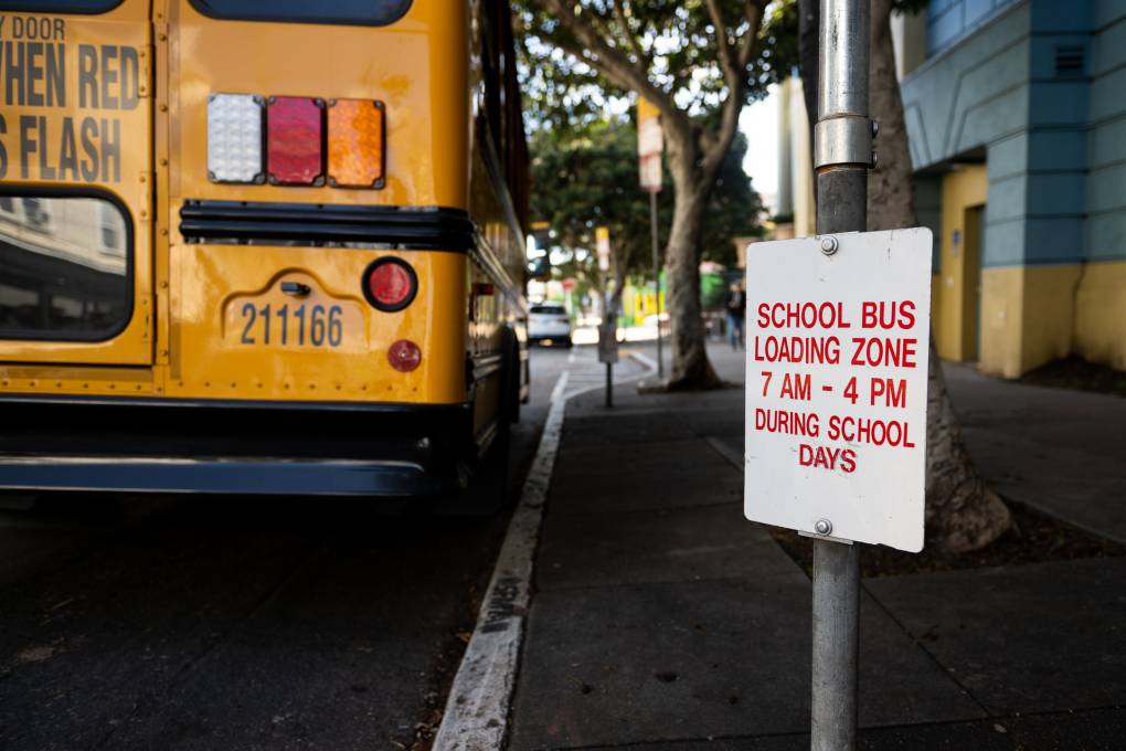 A school bus parked on a street next to a sign that reads "school bus loading zone."