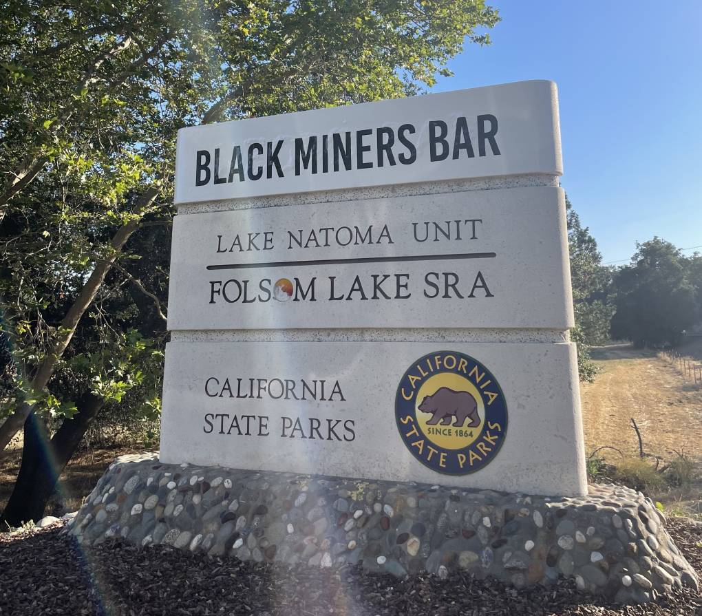 A cement California State Park sign that reads: Black Miners Bar, Lake Natoma Unit, Folsom Lake state recreation area.