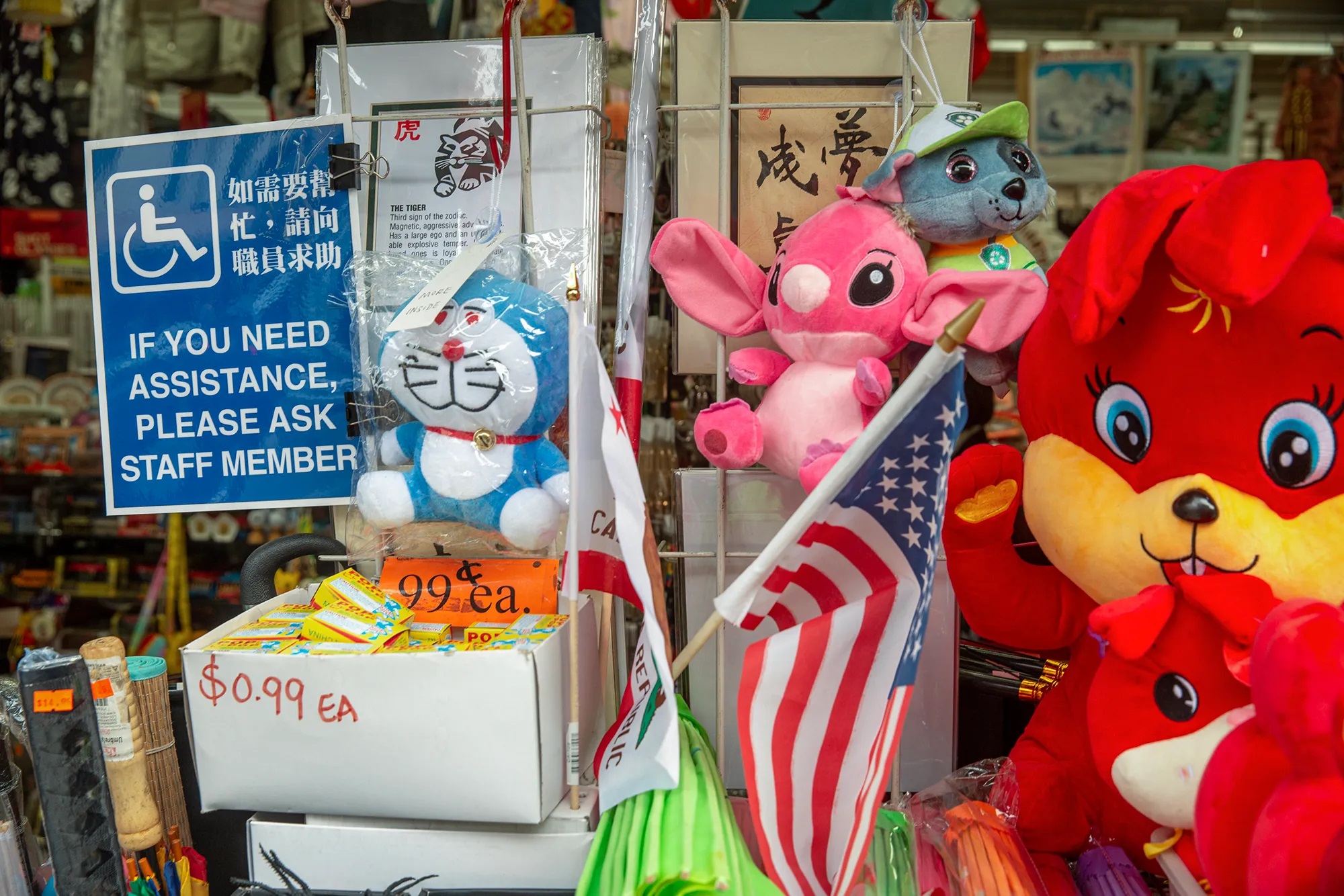 A blue accessibility sign hangs in the window of a building's entrance next to a variety of colorful, stuffed animals on display.