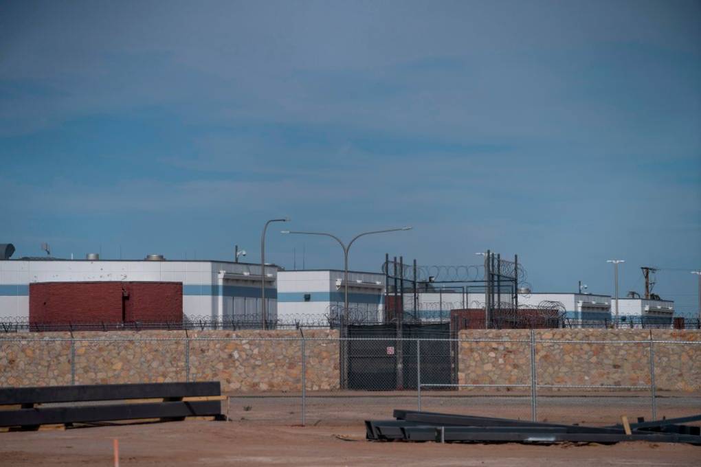 The outside view of a large detention facility, surrounded by walls and tall fencing.