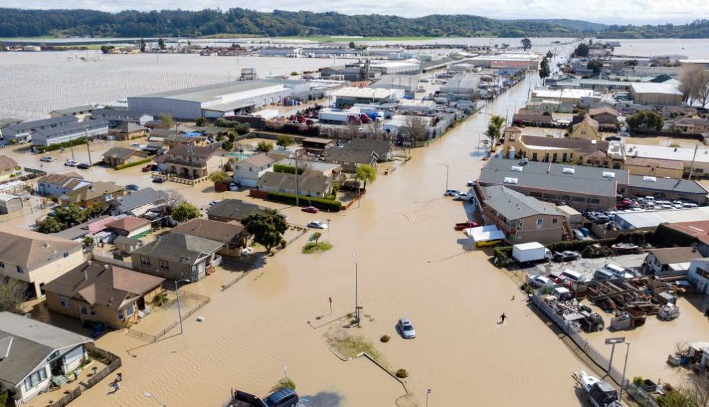 An aerial image of a flooded town with partially submerged houses and cars in brown flood waters.