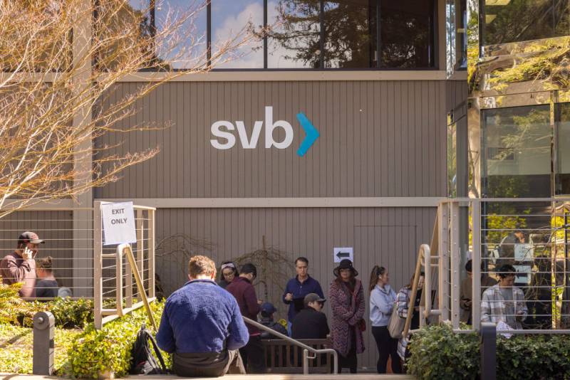 People stand in line outside a building with the "svb" — Silicon Valley Bank — logo.