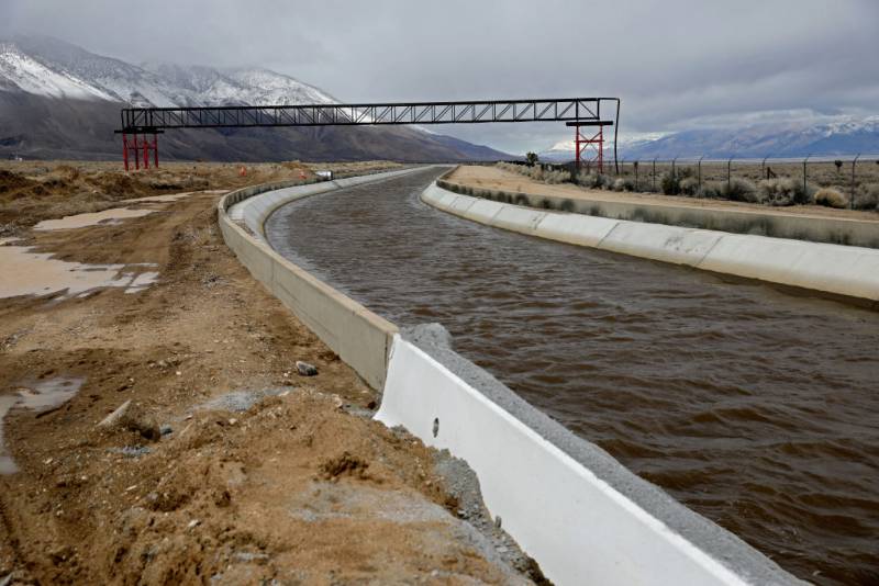 A view of an aquaduct full of water with snow-covered peaks in the distance and clouds overhead.
