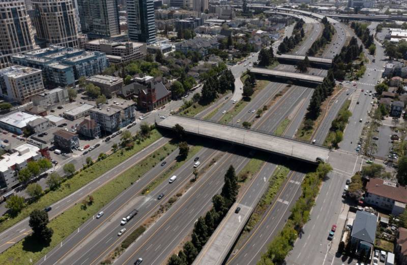 An aerial drone shot of a huge multilane freeway cutting through a dense urban setting.