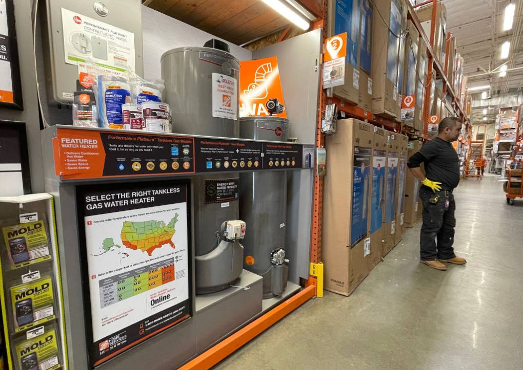 Gas-powered water heaters displayed for sale in a Home Depot store, with an employee standing by.