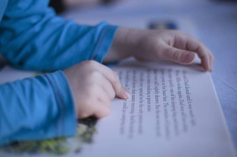 A child reads an open book, pointing at words on a page.