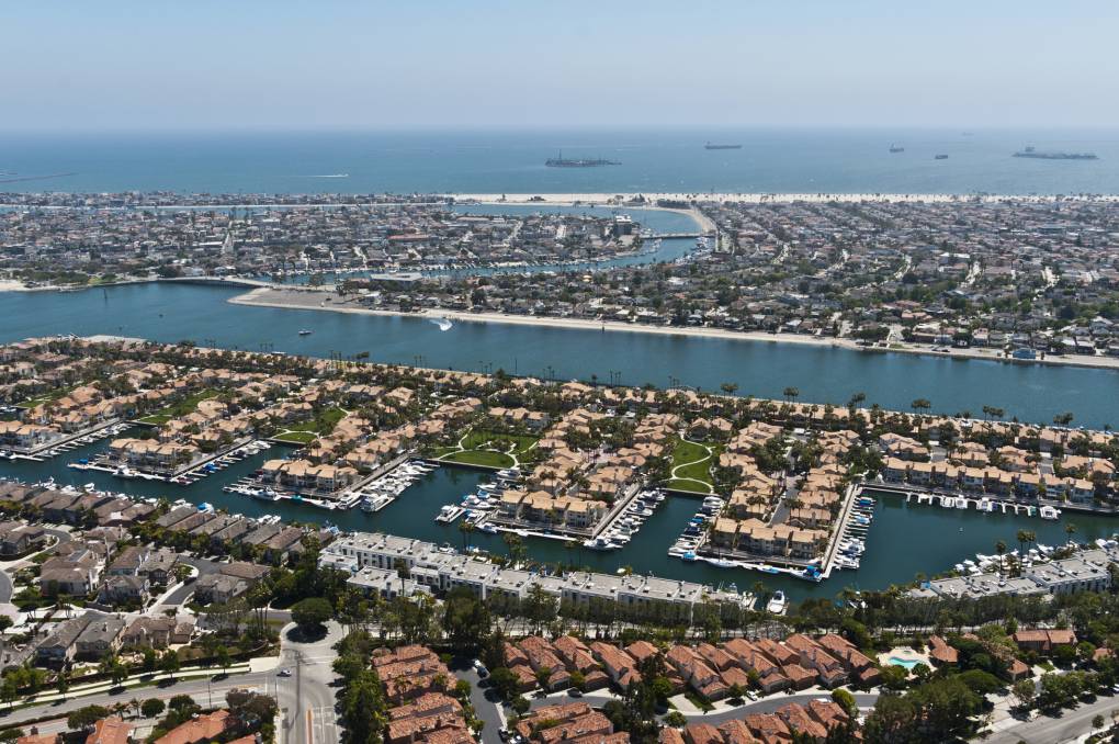 An aerial view of housing along a canal waterway with the beach and ocean in the background.