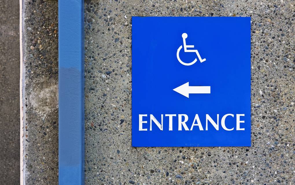 A blue and white disability access sign with white arrow points toward an entrance to the left.