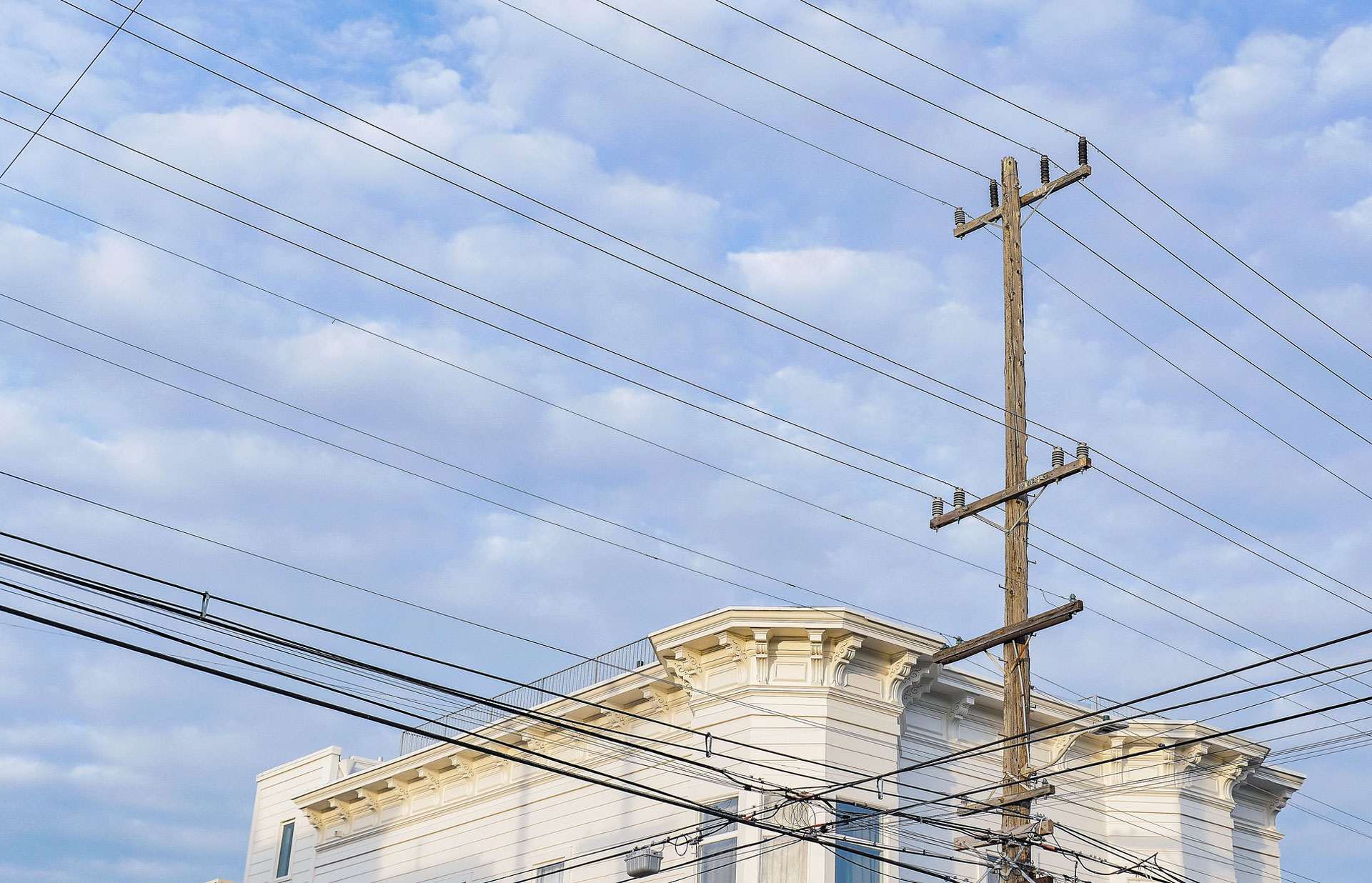 A photo shows primarily a wooden power pole with utility lines crossing the sky, and the outline of the top of a building that looks like a San Francisco victorian in the background