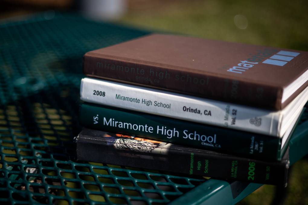 Four different colored books that say "Miramonte High School" on the side are stacked on a green bench seat.
