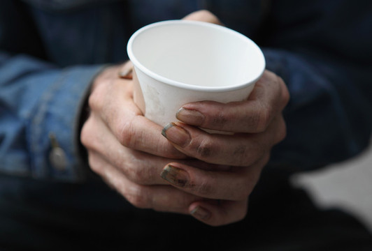 Two white hands with dirt and long fingernails clasp a white coffee cup.
