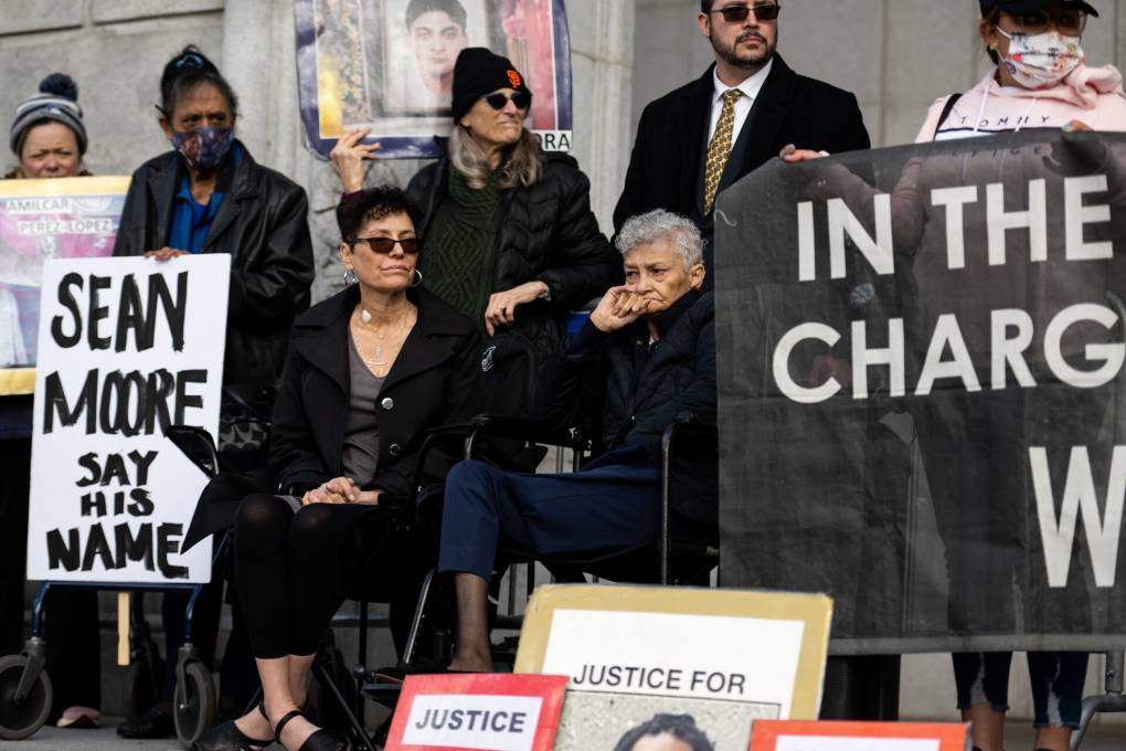 Various people sit on the top of the steps leading to a courthouse with signs and photos, in center is April Green and Judy O'Neill