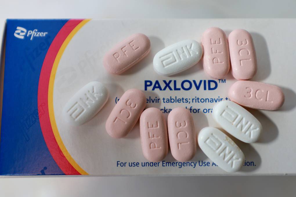 A box of the COVID antiviral treatment Paxlovid photographed from above, with several pink and white pills scattered on the box.