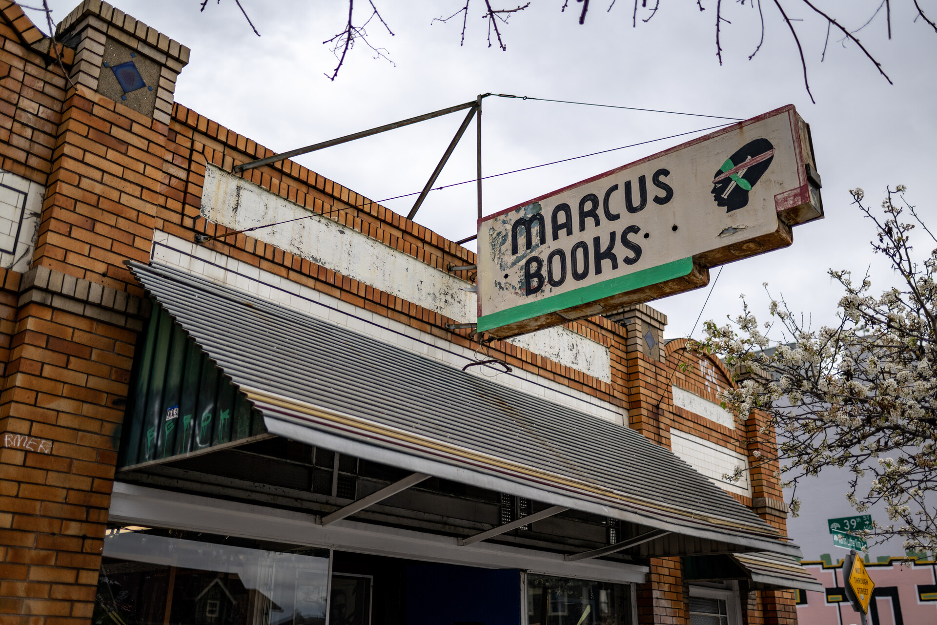 A sign hangs outside of a brick building reads "Marcus Books."