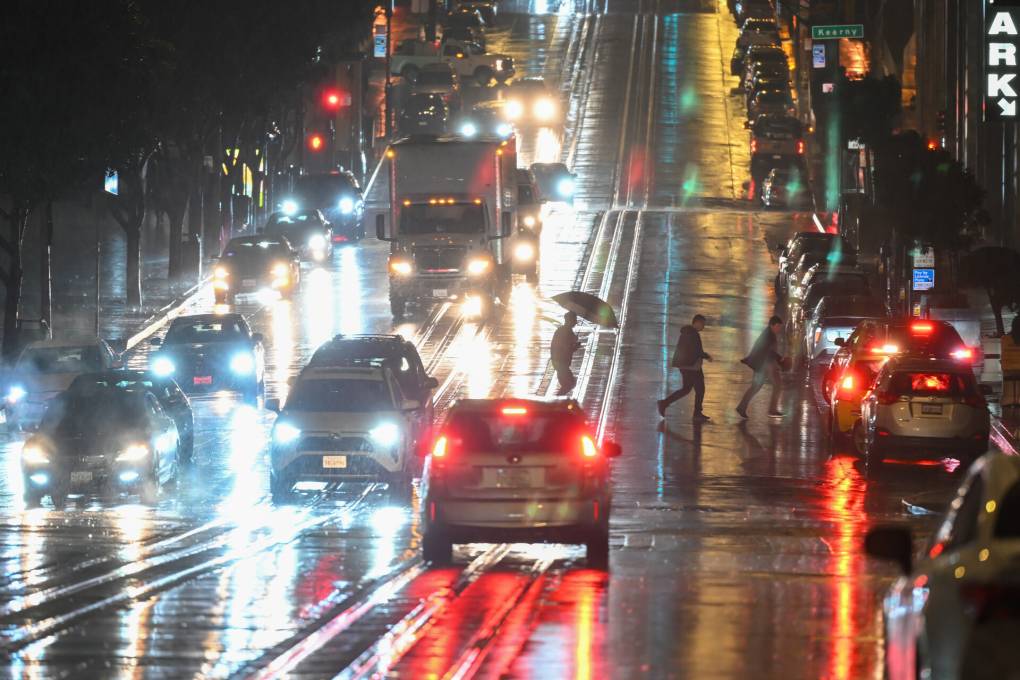 A photograph of a wet, rainy city street at night, with car headlamps blurred by the rain