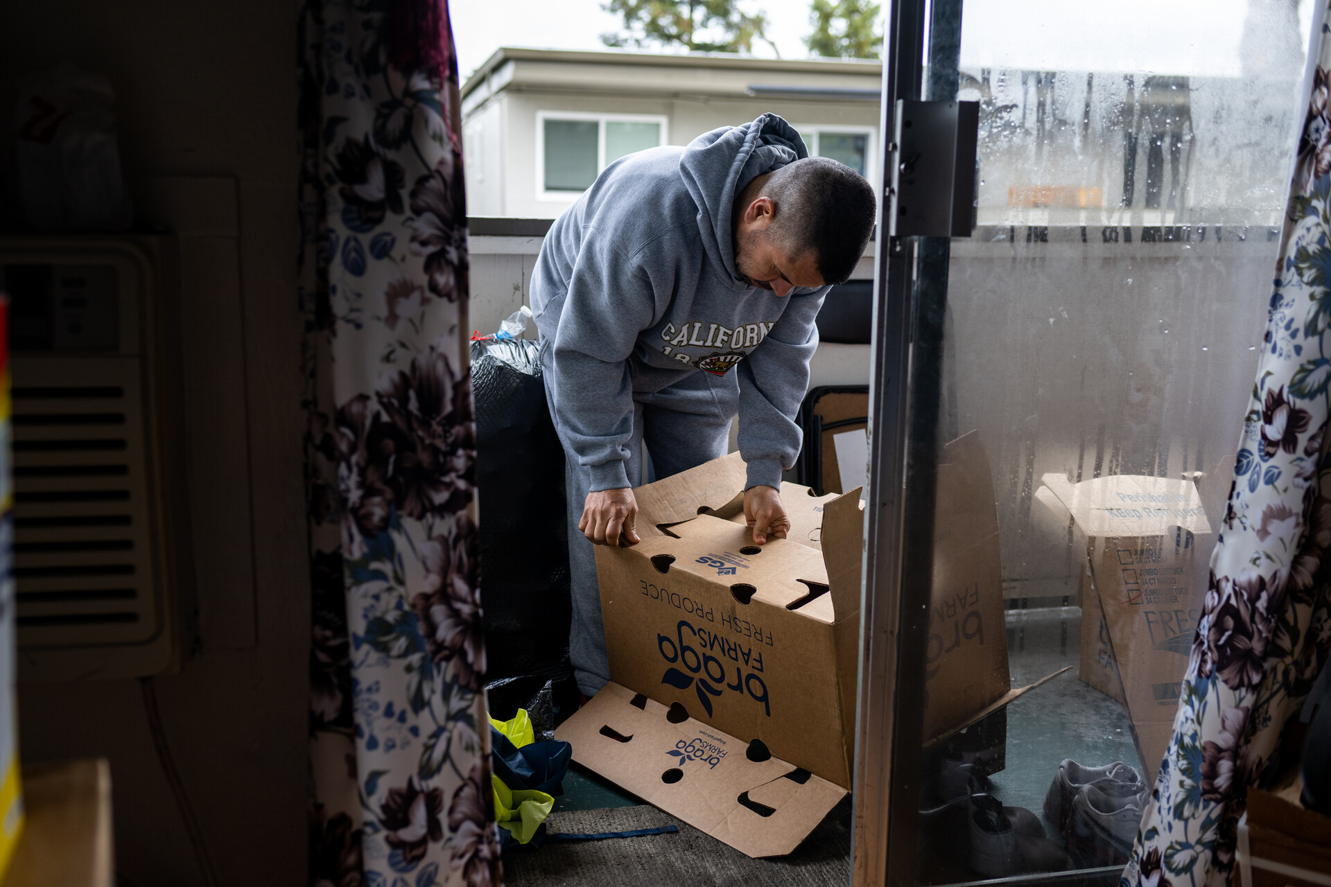 A man on the patio of his apartment leaves the sliding glass door ajar as he puts together boxes getting ready to move out.
