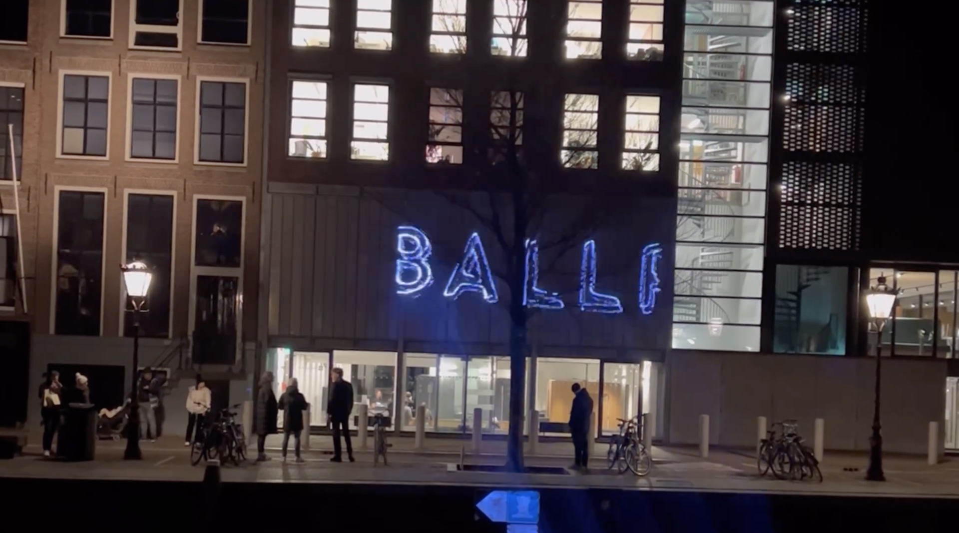 A screenshot from video showing a laser projection on a building wall that says "Ballp."