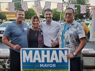 Three men and one woman post for a photo outside, holding a sign that says 'Mahan Mayor.'