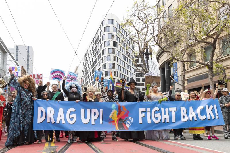 A crowd of people hold a banner that reads "Drag Up! Fight Back!"