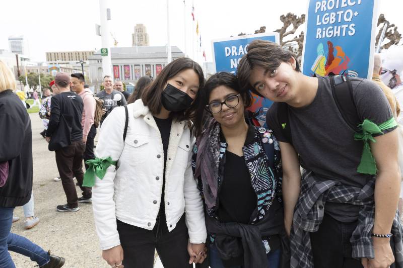 An Asian woman with a face mask, a south Asian woman and an Asian man smiles for the camera with people behind them.