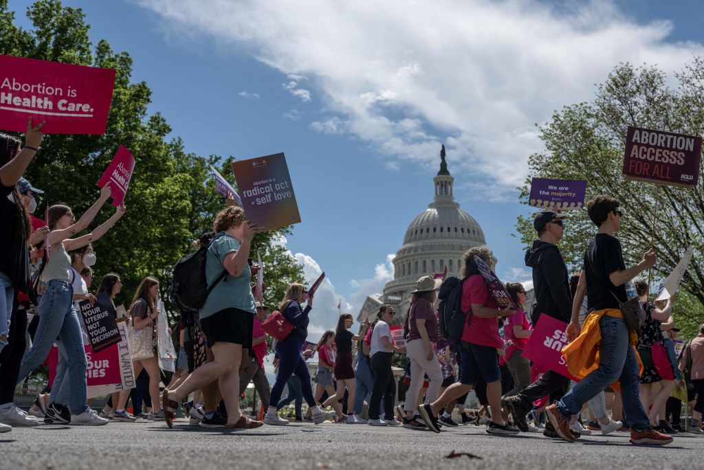 Protesters march holding signs that read "Abortion Is Health Care" with the U.S. Capitol in the backdrop.
