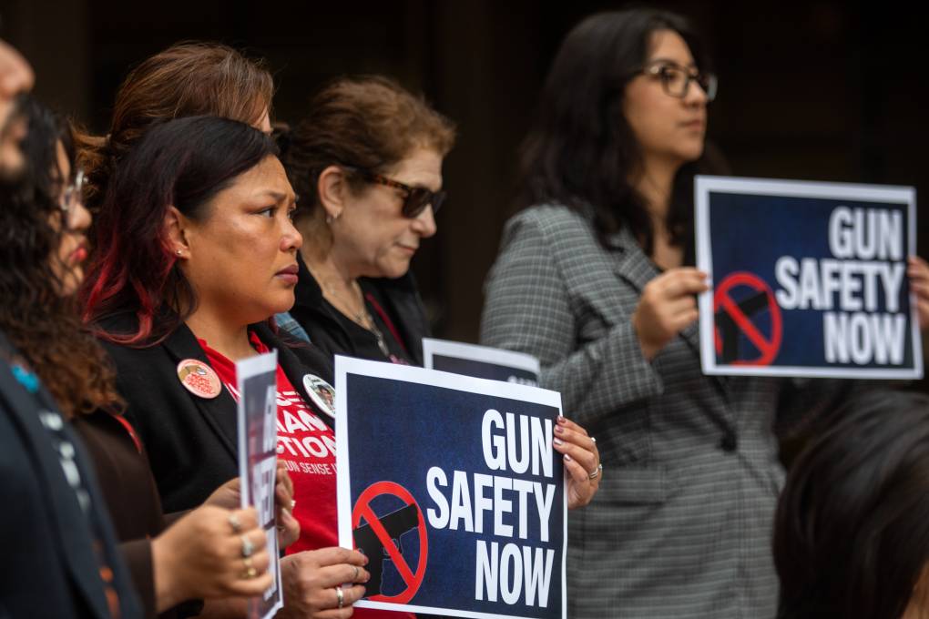 A crowd of solemn faces hold signs that read, "Gun Safety Now."
