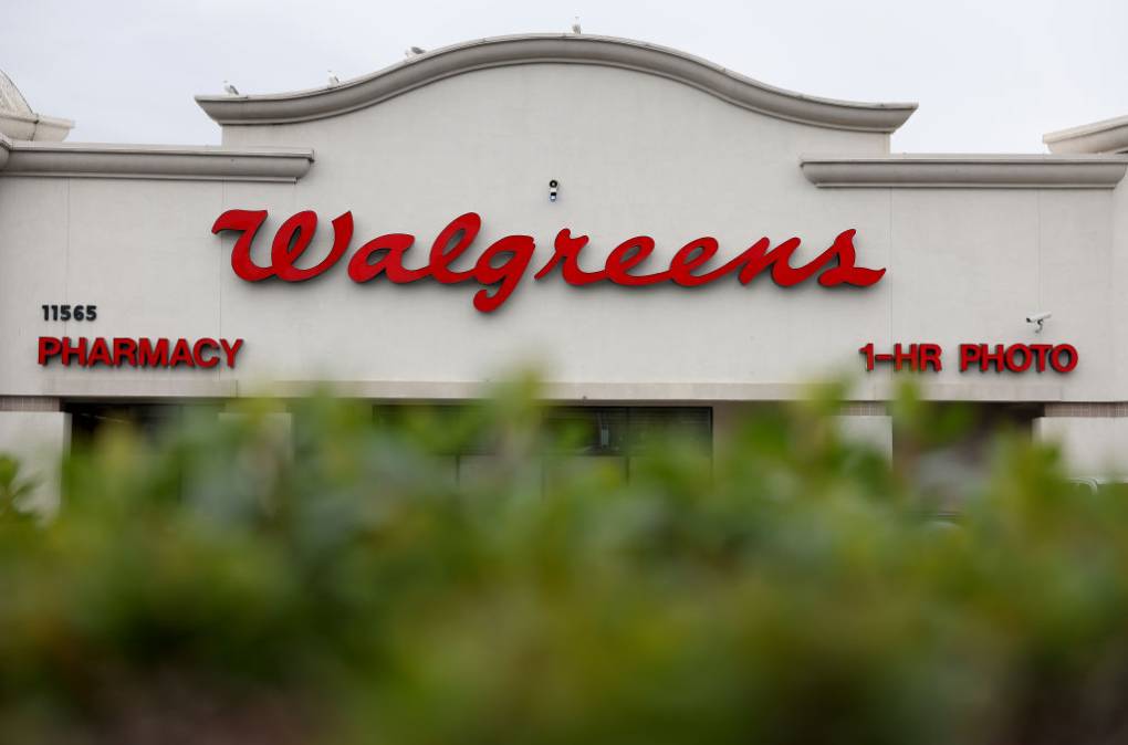 A building sign that reads "Walgreens" with "Pharmacy" and "1-HR Photo" on the left and right sides with a bush in the foreground.