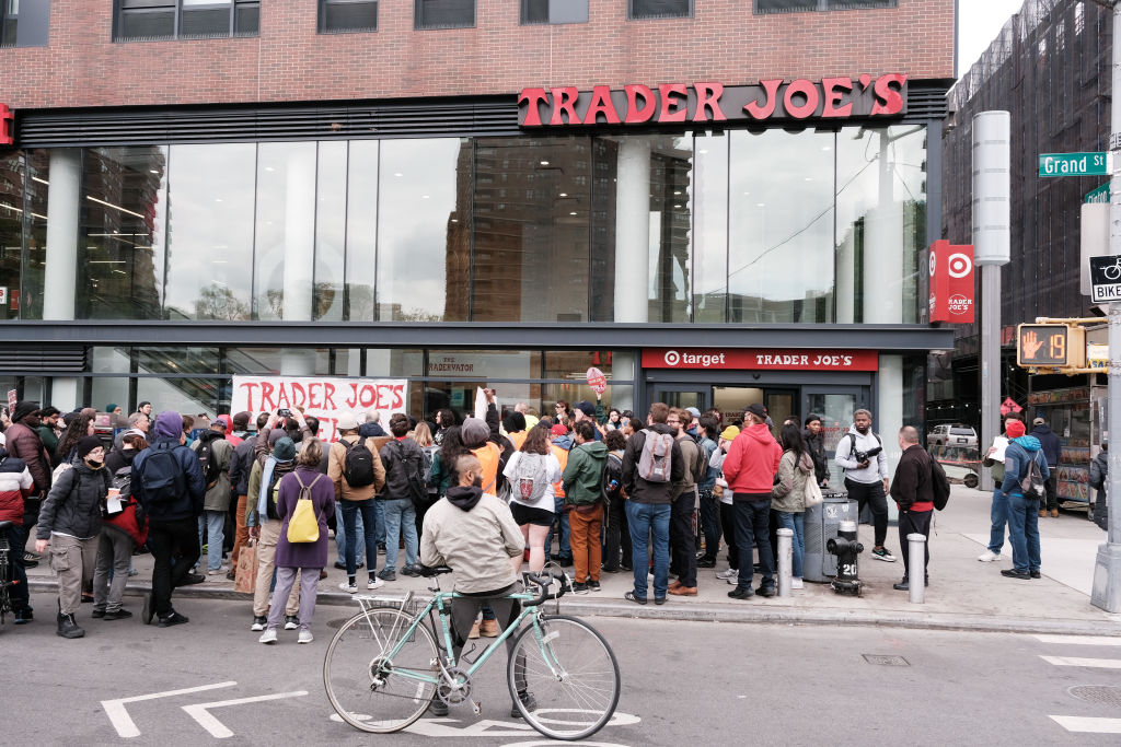 A crowd of protesters gathered outside a Trader Joe's store on a city street.