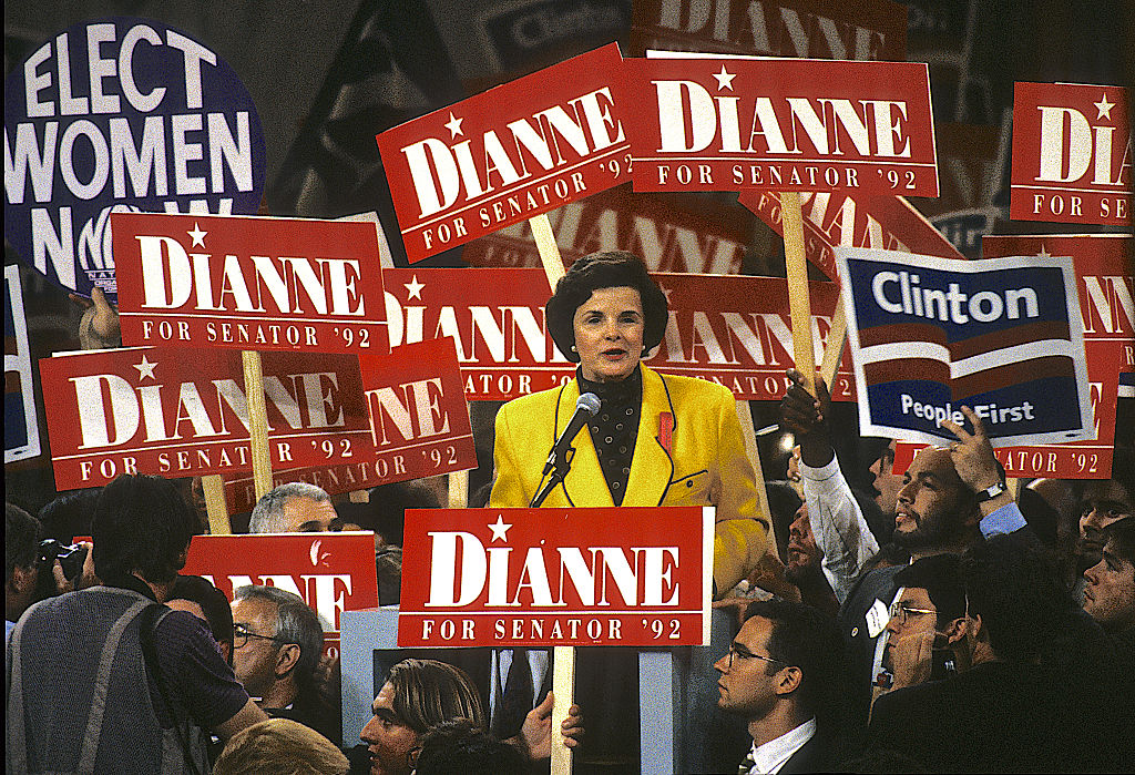 A white woman speaks to supporters at a convention with signs around her that read "Dianne"