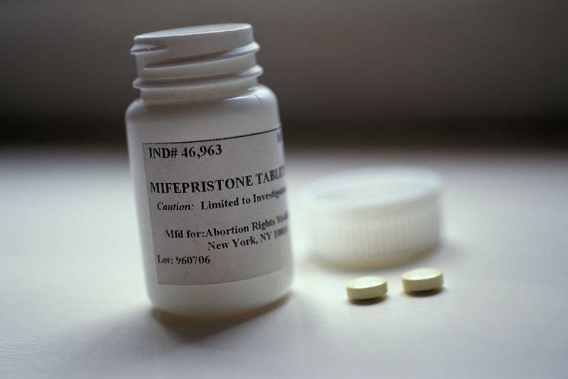 Two pills sitting beside a pill box with 'mifepristone' written on the box.