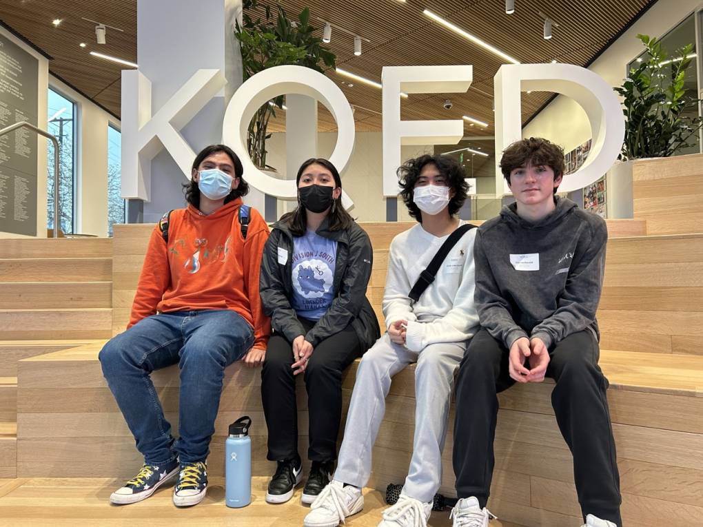 Four teenagers sit on large wooden steps in the lobby of KQED Studios