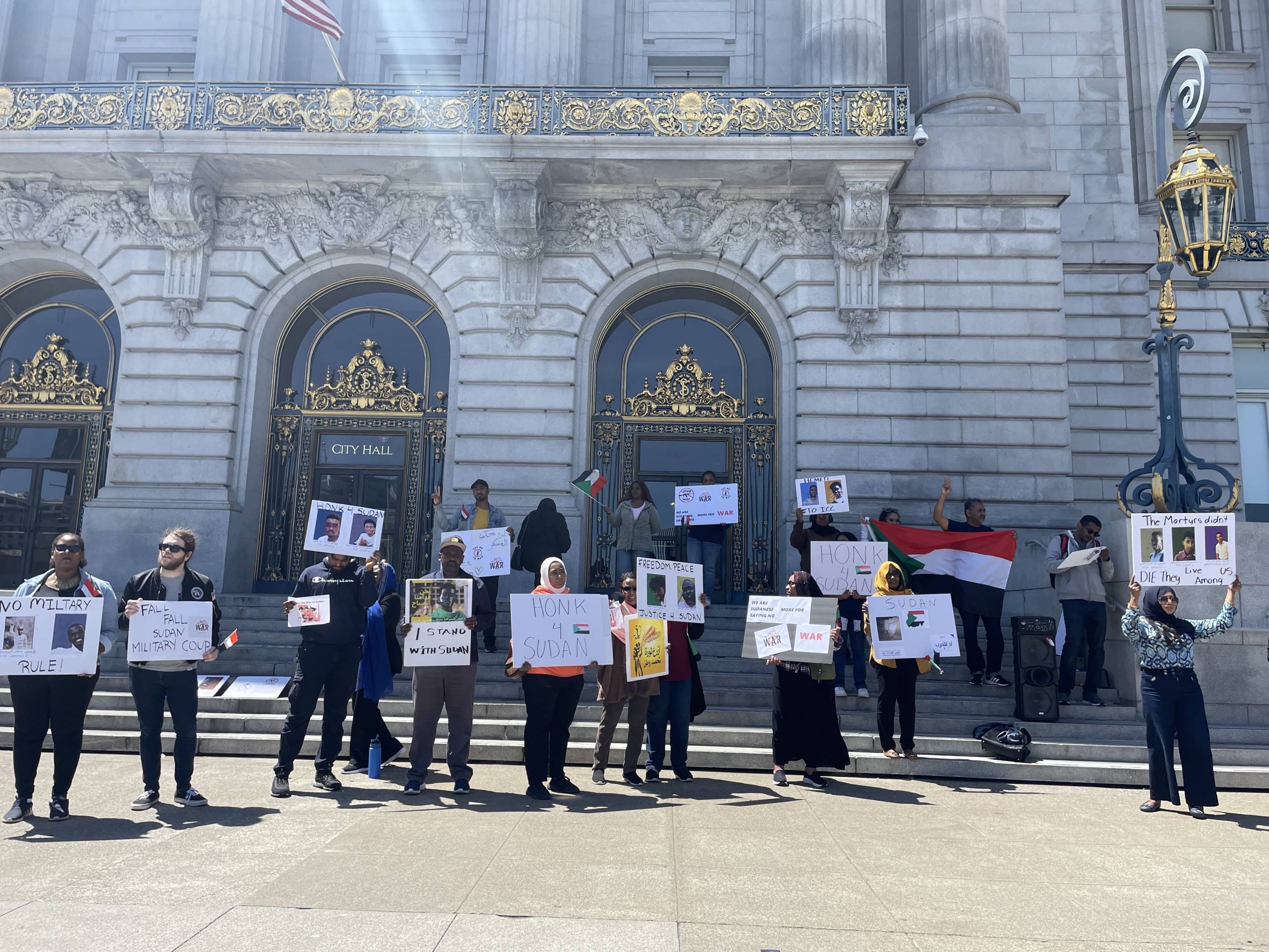 Various Sudanese American protesters hold signs outside SF City Hall.