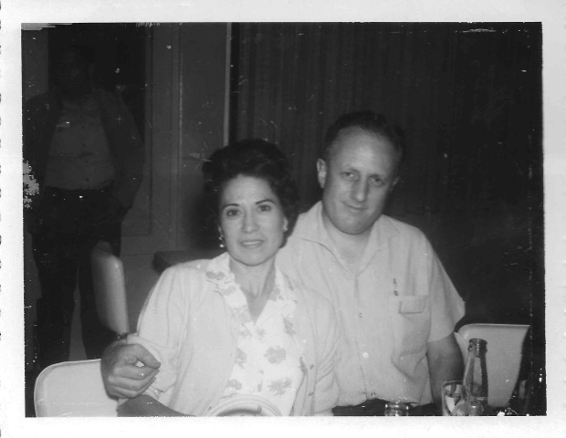 A vintage black and white photo of a woman and man sitting down with the man's hand around the woman's arm.