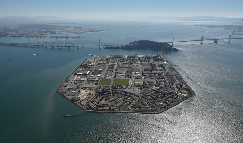 A view of Treasure Island from up above with blue water surrounding it and the Bay Bridge in the background.