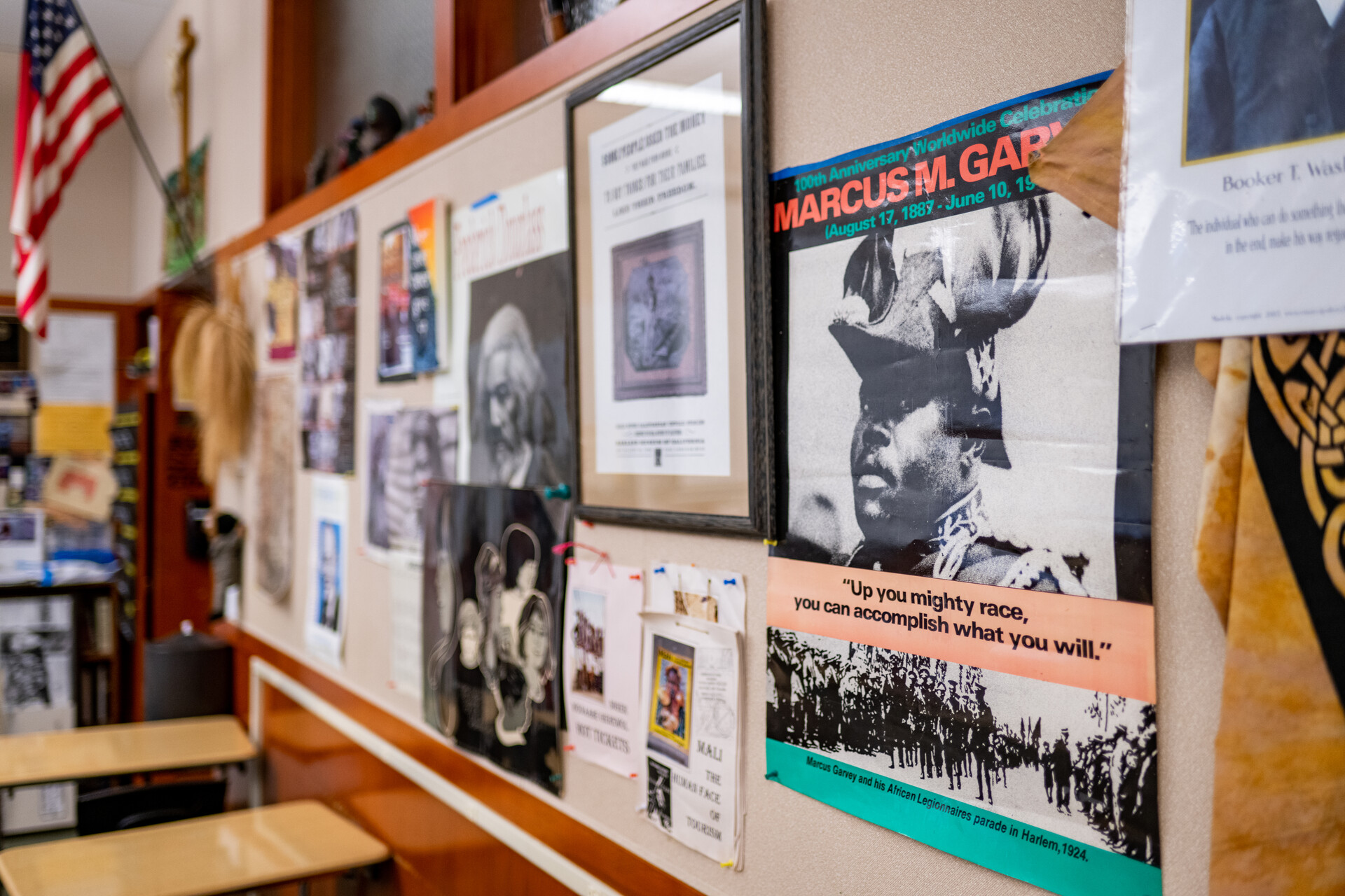 Dozens of black and white as well as colorful posters depict Black historical figures with inspirational quotes. These line the wall of a classroom where desks are neatly in rows.