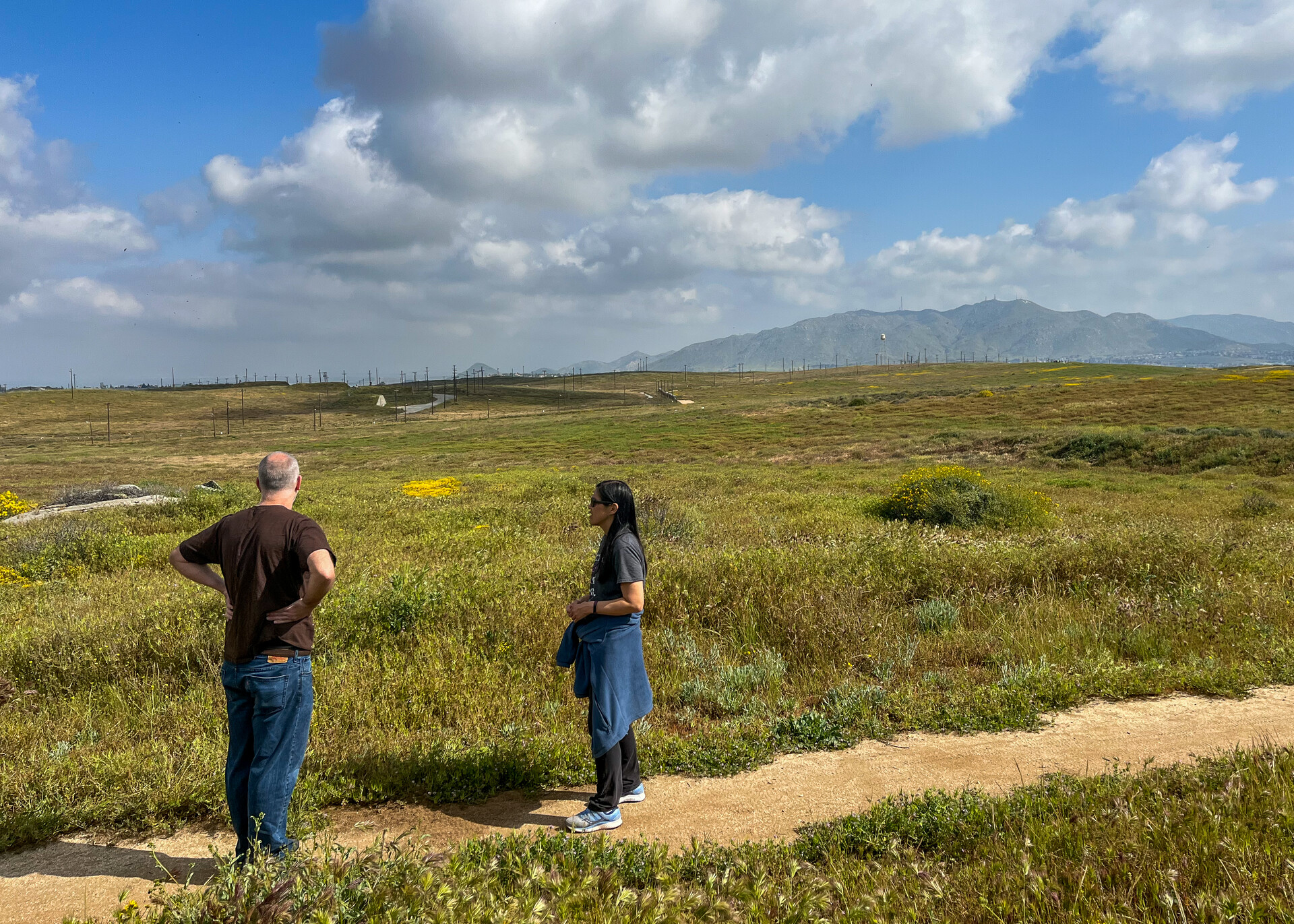 A man and a woman, with their backs to the camera, stand on a path looking out on a large expanse of grassland .