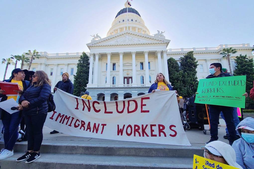 People hold up a sign in front of the state Capitol that reads, "Include Immigrant Workers"