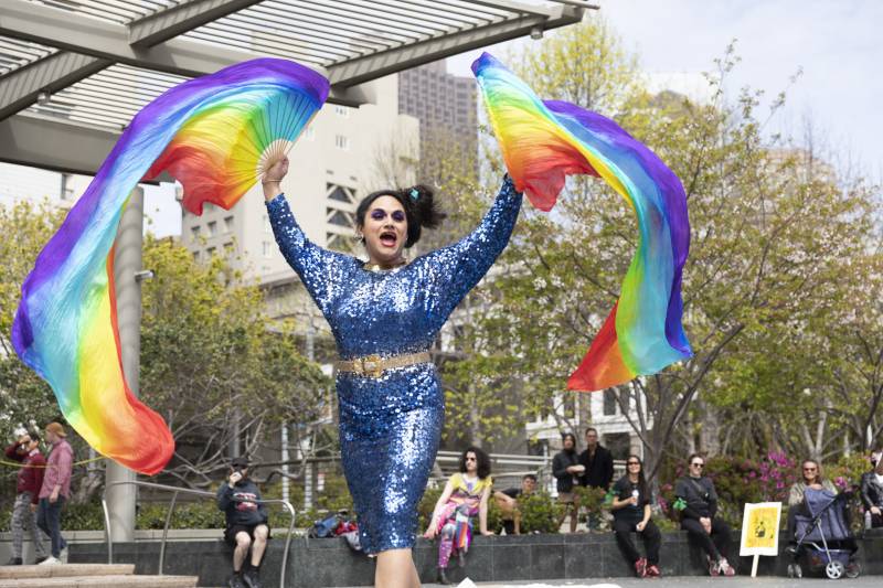 A trans person on stage performs in drag with rainbow wings.