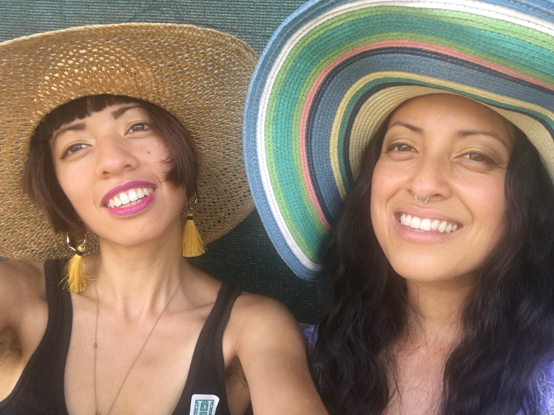Two sisters wear large, straw sun hats and smile for the camera.