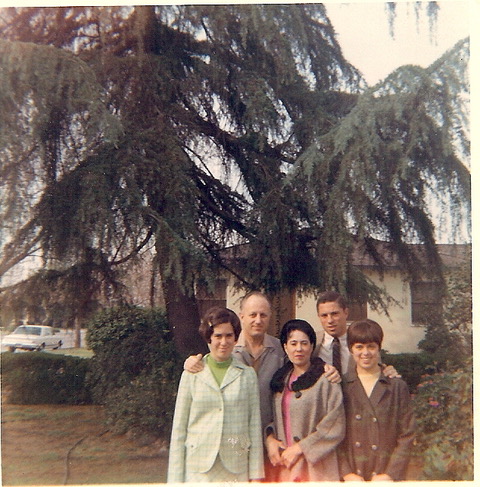 A vintage photo of three women standing in front of two men with trees and a building in the background.