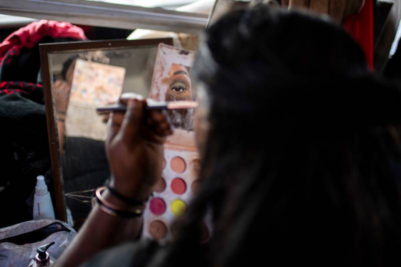 An African American woman applies eye makeup in a mirror.