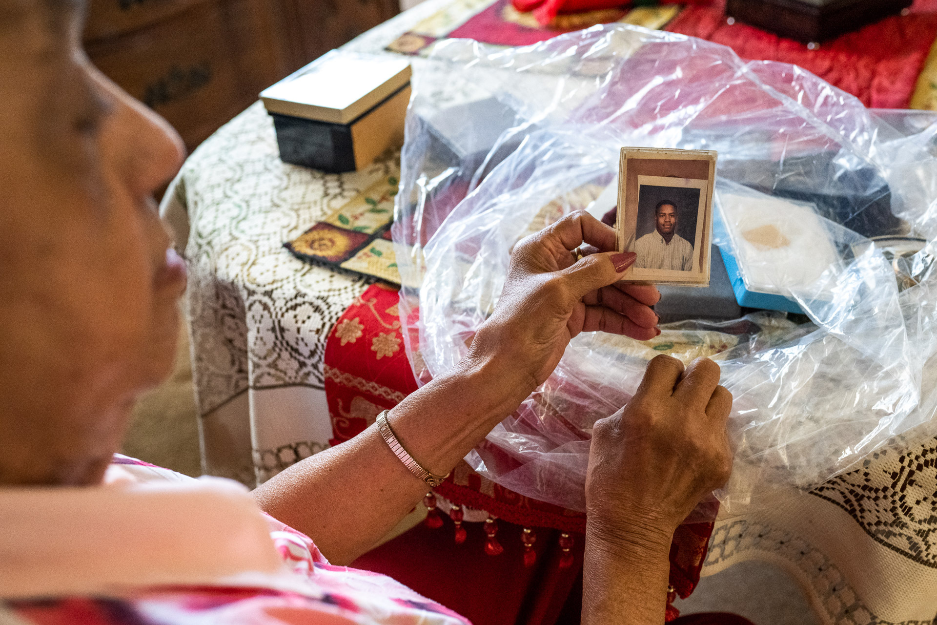 An African American woman looks at a photo of a young African American man while seated at a table at home.