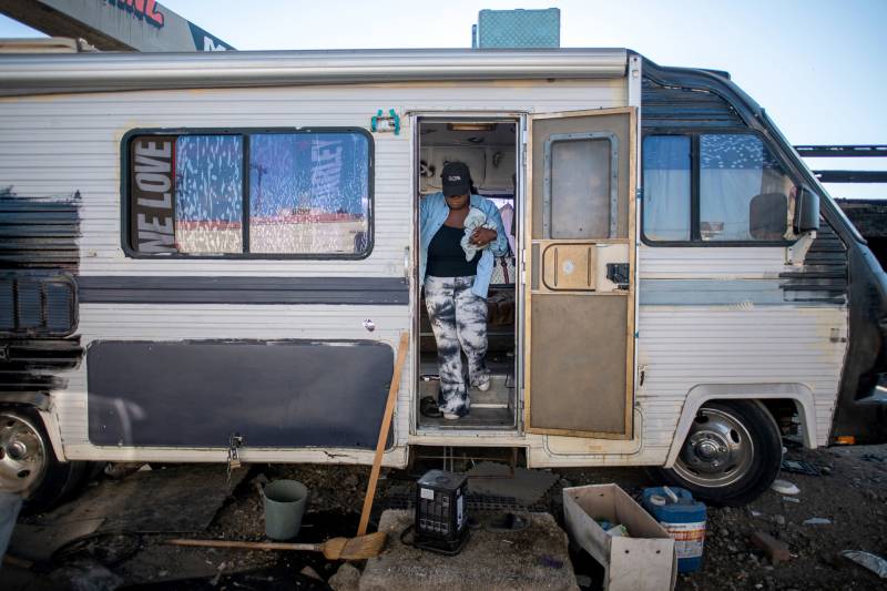 An African American woman leaves her RV as she prepares to exit the open door and down the stairs.